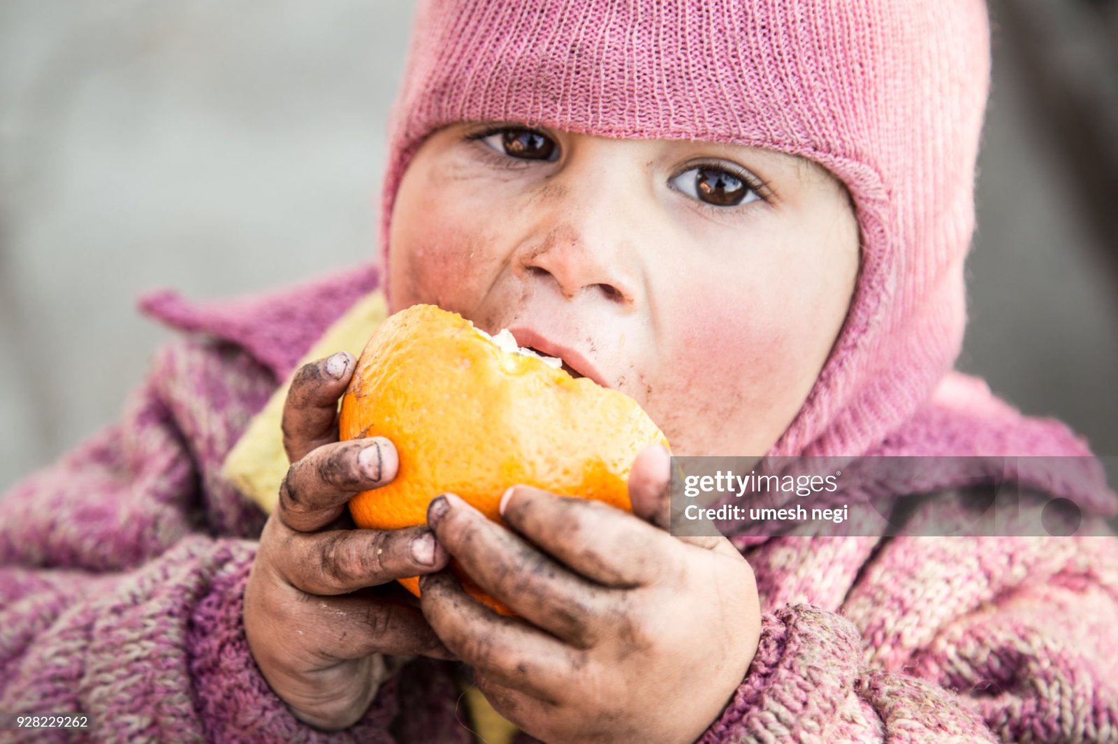 indian baby eating oranges with dirty hand, looking directly at camera